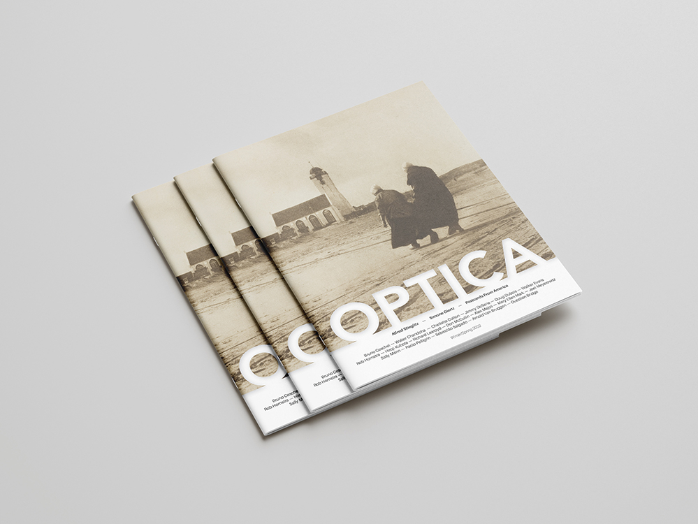 The cover of Optica Magazine. It's cover is dominated by a monochrome photograph of two people and a large building.